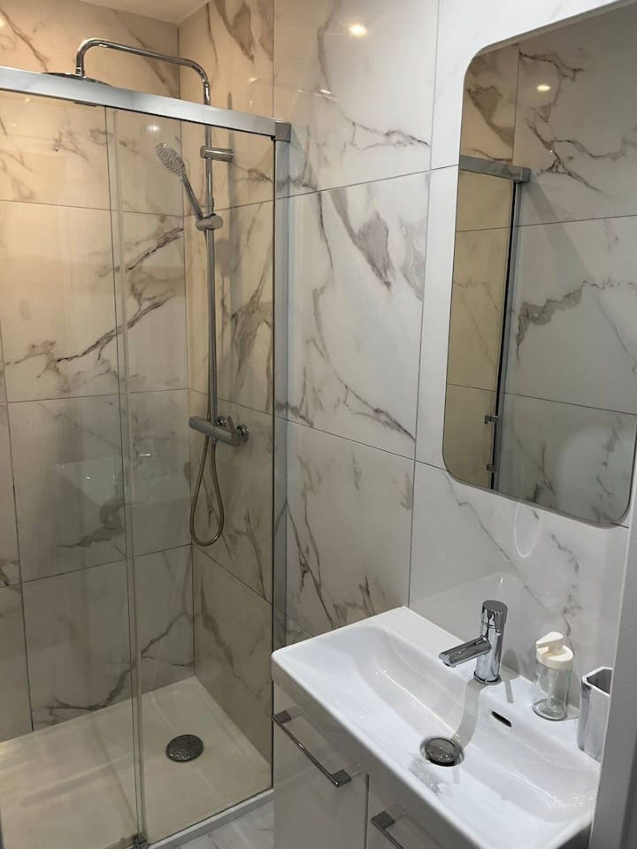 Une salle de bain avec une douche à parois de verre, un lavabo blanc et un miroir.