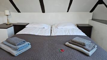 A neatly made bed with white linens and a grey quilt, flanked by two nightstands with lamps, in a room with a simple, modern design.