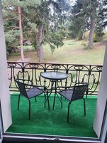 Un balcón con suelo de césped artificial verde, dos sillas de metal negro y una pequeña mesa redonda.