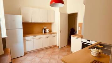 Een kleine keuken met witte kasten, een rode hanglamp en een klein aanrecht met een theepot.
