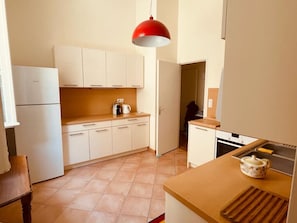 Een kleine keuken met witte kasten, een rode hanglamp en een klein aanrecht met een theepot.