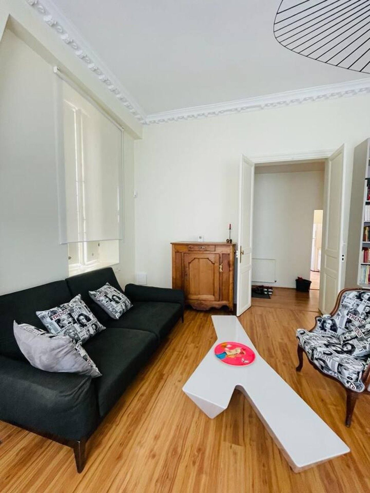 Een woonkamer met een zwarte bank, een witte salontafel en een fauteuil met een patroon.