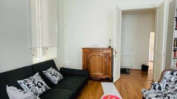 Een woonkamer met een zwarte bank, een witte salontafel en een fauteuil met een patroon.