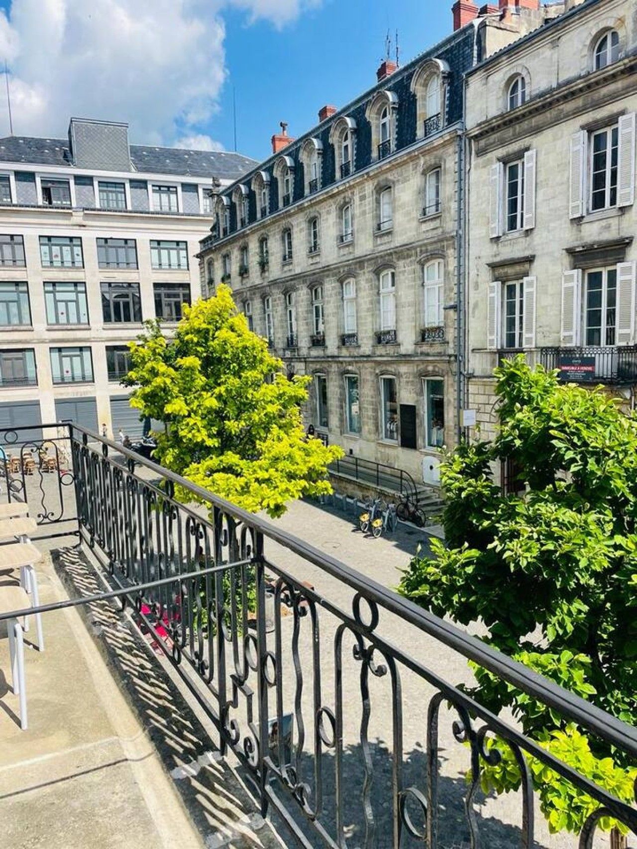 A balcony with wrought iron railings overlooking a street with historic buildings and a tree.