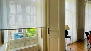 Een kamer met een groot raam, een radiator, een deur en een stoel.
