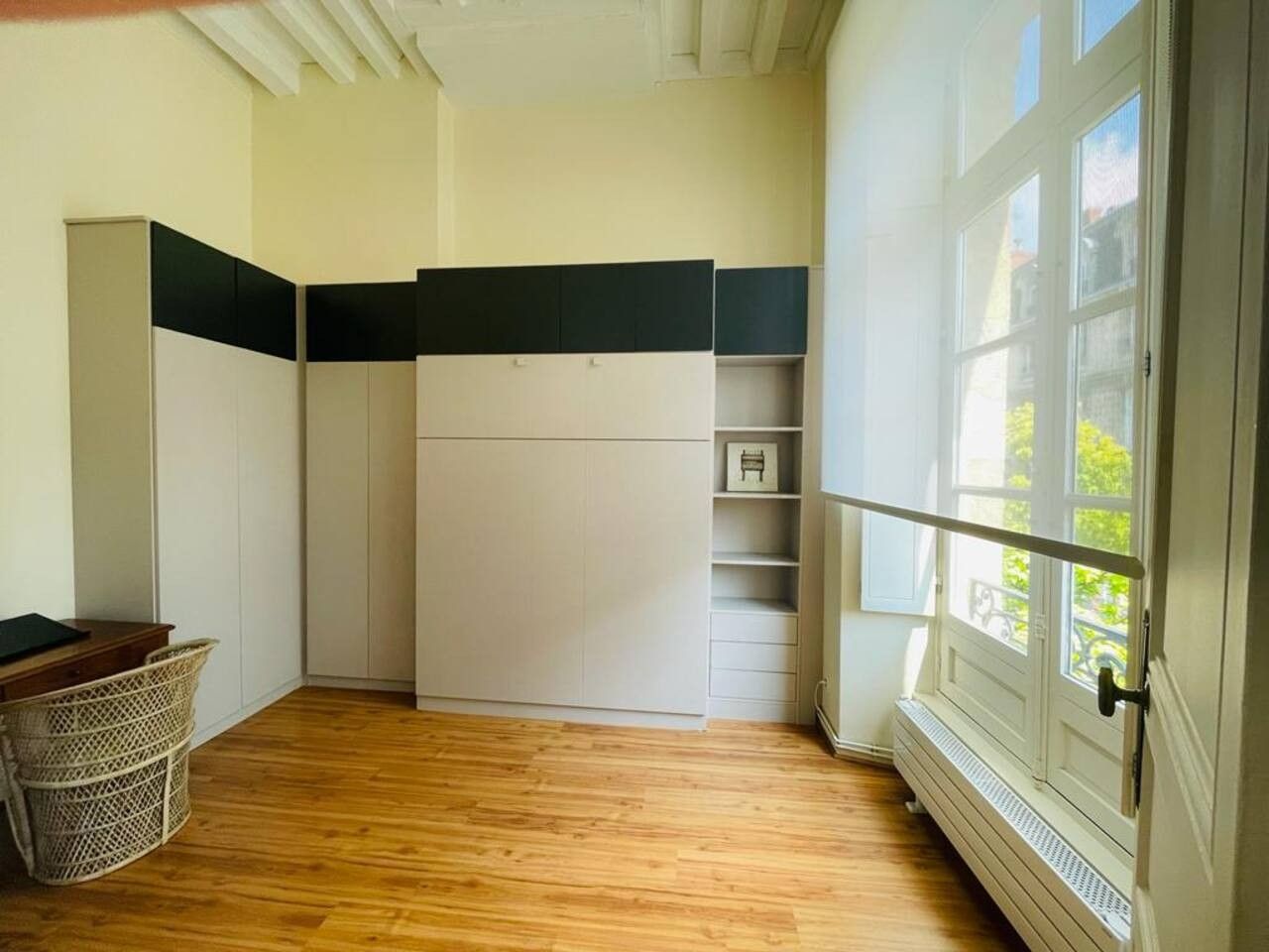 Habitación compacta con armario blanco empotrado, una pequeña mesa de madera y ventana con vistas al verdor.