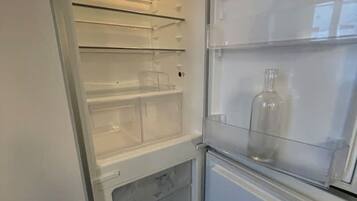 Ein offener Kühlschrank mit mehreren Einlegeböden und einer Glasflasche auf der obersten Ablage.