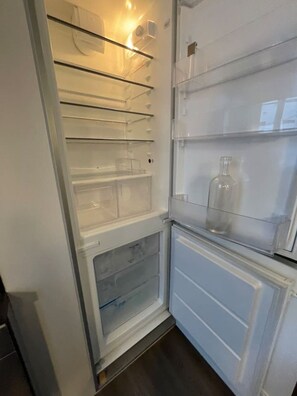 Ein offener Kühlschrank mit mehreren Einlegeböden und einer Glasflasche auf der obersten Ablage.