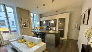 Una sala de estar moderna con un sofá blanco, una zona de cocina con isla central y un comedor.