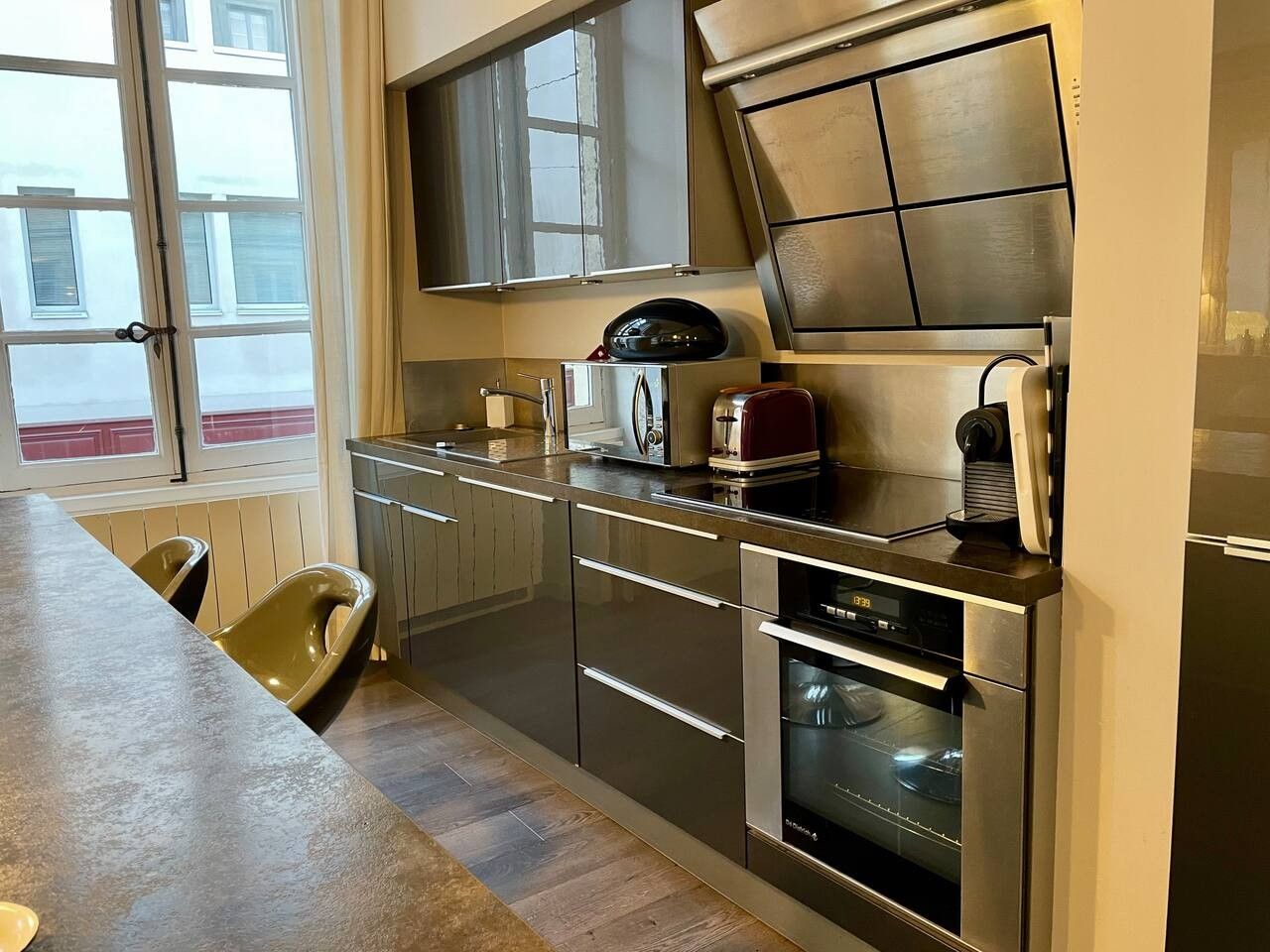 A modern kitchen with stainless steel appliances, a built-in oven, and a window overlooking the street.
