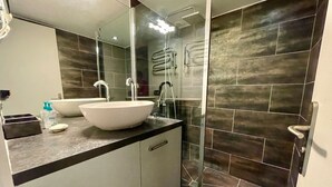 Un baño moderno con un lavamanos grande de color blanco, un espejo y una zona de ducha con puerta de cristal.