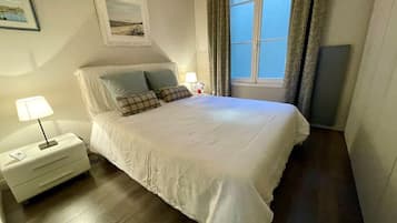 Ein Schlafzimmer mit einem Bett, Nachttischen, einer Lampe, einem Fenster mit Vorhängen und Wandkunst.
