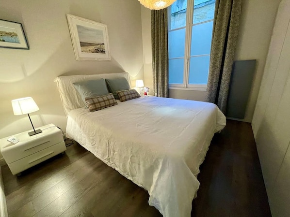 Ein Schlafzimmer mit einem Bett, Nachttischen, einer Lampe, einem Fenster mit Vorhängen und Wandkunst.