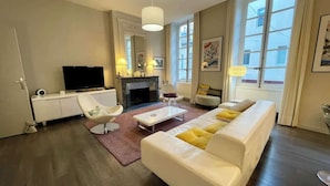 A modern living room with a white sofa, a flat-screen TV, a fireplace, and large windows.