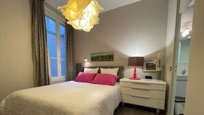 Un dormitorio con cama, mesita de noche, lámpara y ventana con cortinas.