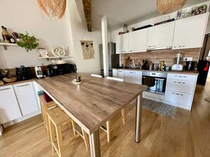 A modern kitchen with white cabinets, a wooden dining table, and stainless steel appliances. - Rooftop dans hyper centre (Bordeaux)
