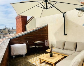 Una terraza en la azotea con una mesa de madera, un sofá y una sombrilla grande que da sombra.
