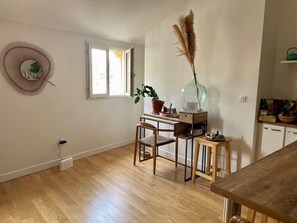 A room with a wooden floor, a desk with a chair, a potted plant, a vase with pampas grass, and a window.