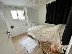 Una camera da letto con un letto, una finestra, un termosifone, un tappeto bianco e una sedia in vimini.