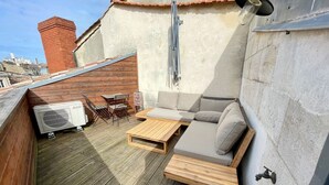 Een terras op het dak met een houten dek, een bank, een tafel en een airconditioning.