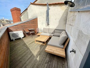 Una terrazza sul tetto con pavimento in legno, un divano, un tavolo e un condizionatore.