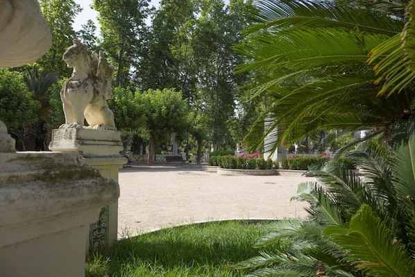 Estátua de leão em um jardim com palmeiras e um banco.