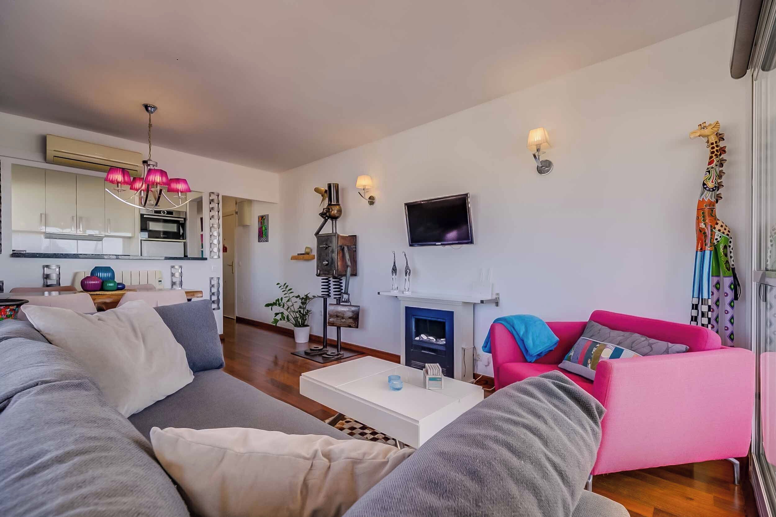 A modern living room with a grey sofa, a pink armchair, a white coffee table, and a fireplace.