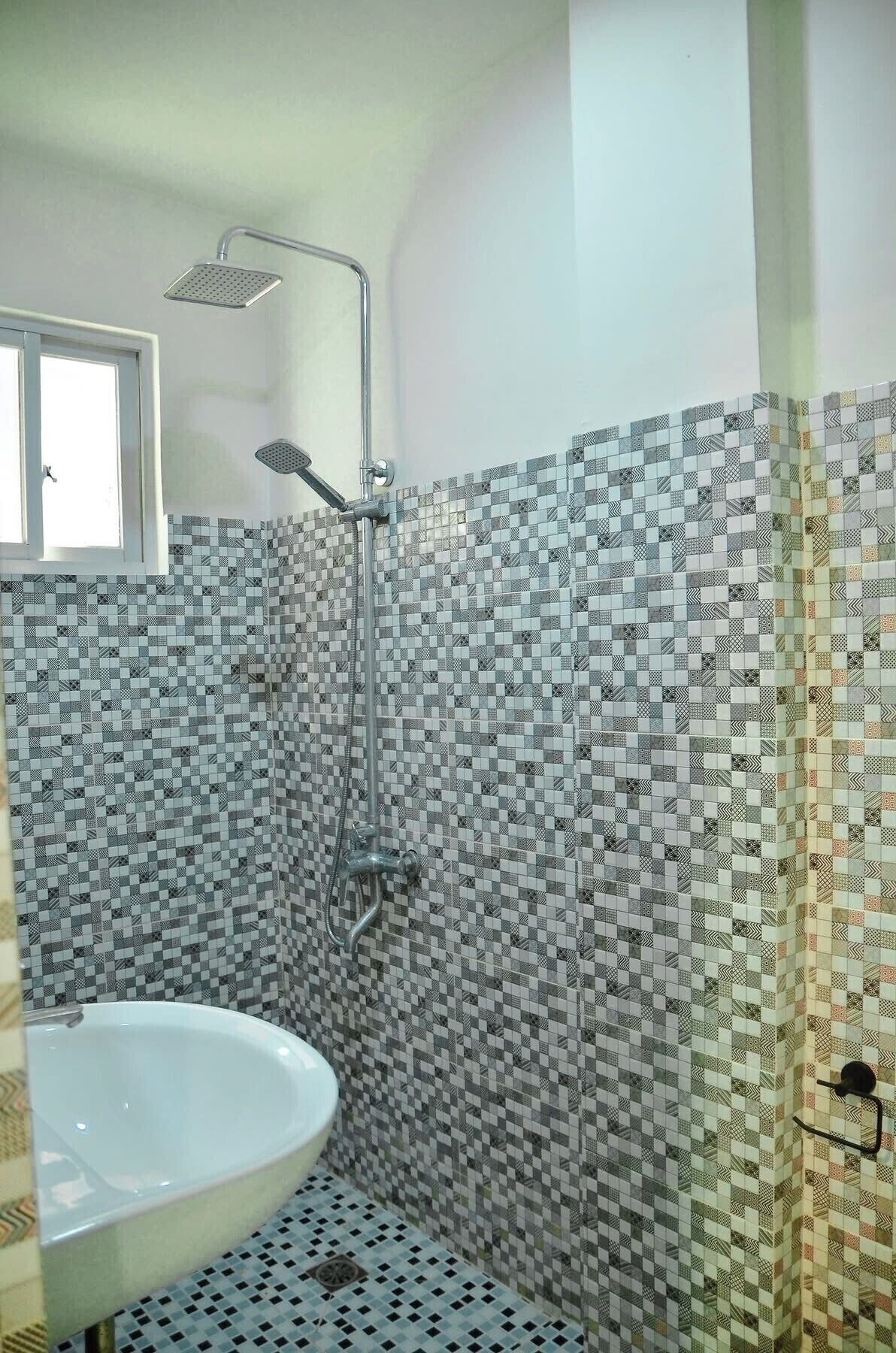 Un baño con lavamanos blanco, ducha con cabezal de ducha manual y pared de azulejos estampados.