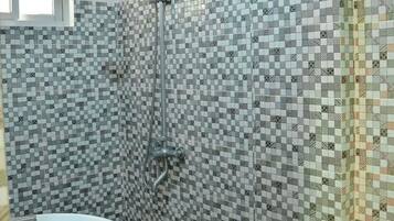 Un baño con lavamanos blanco, ducha con cabezal de ducha manual y pared de azulejos estampados.