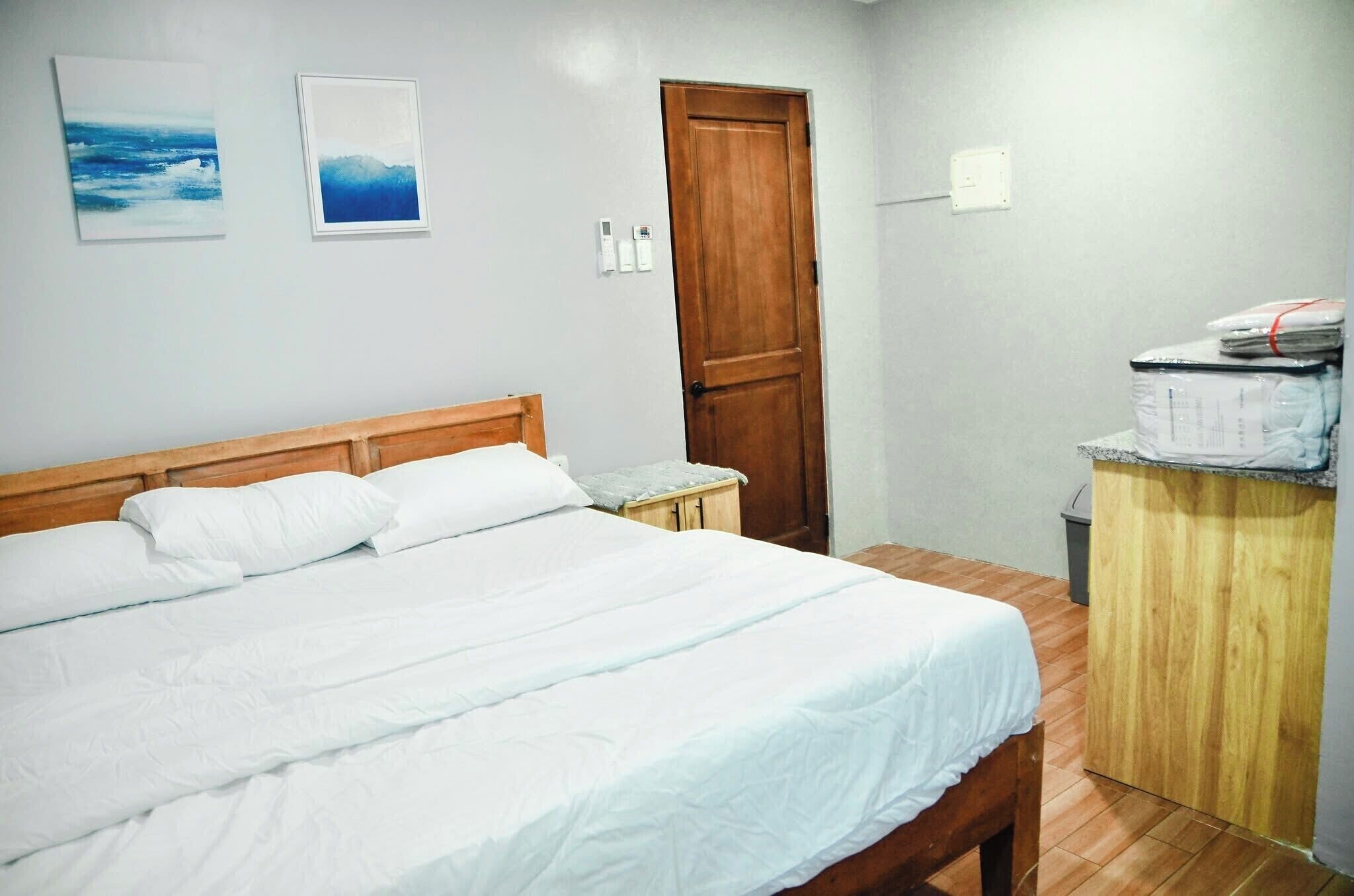 Un dormitorio con una cama de madera, una mesita de noche pequeña, un armario de madera y dos cuadros en la pared.
