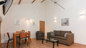 A spacious living room with a brown sofa, a glass coffee table, a dining table with chairs, and a wooden floor. - Strawberry line, flat 2 (Wells)