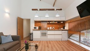 A modern kitchen with a wooden countertop, white cabinets, and a built-in oven. There is a dining area with a glass coffee table and a sofa. - Strawberry line, flat 2 (Wells)