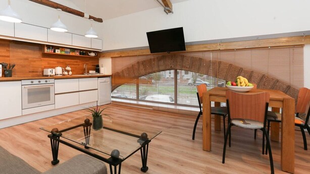 A modern kitchen with white cabinets, a built-in oven, and a dining area with a wooden table and chairs. - Strawberry line, flat 2 (Wells)