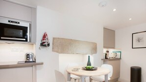 A compact kitchen with a microwave, toaster, and a small dining table with chairs. - The Design Studio Apartment (Bath)