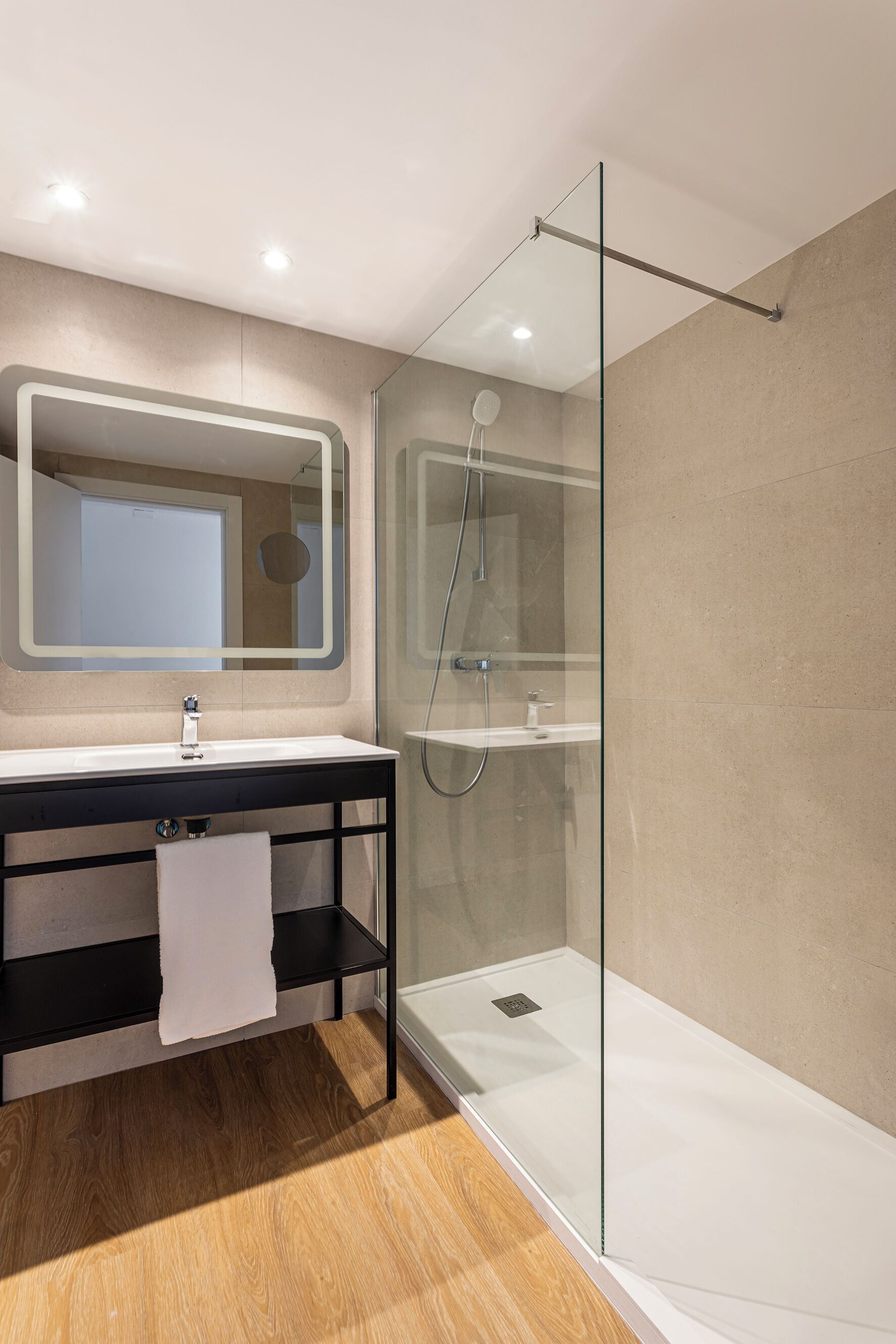 Un bagno moderno con doccia vetrata, un grande specchio e un mobile lavabo in legno.