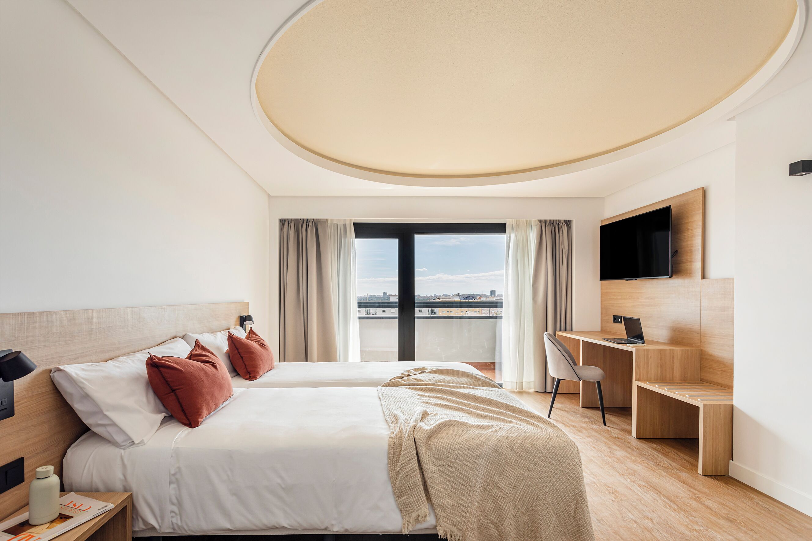 A modern hotel room with two beds, a desk, and a TV.