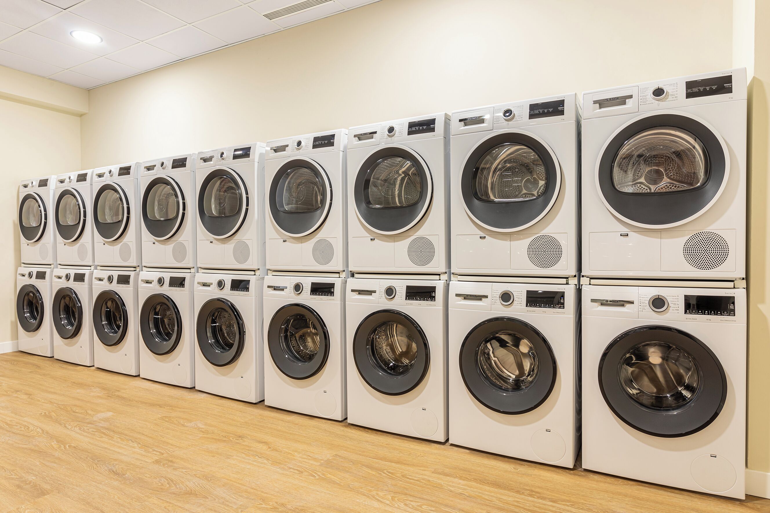 A row of stacked front-loading washing machines in a commercial setting.