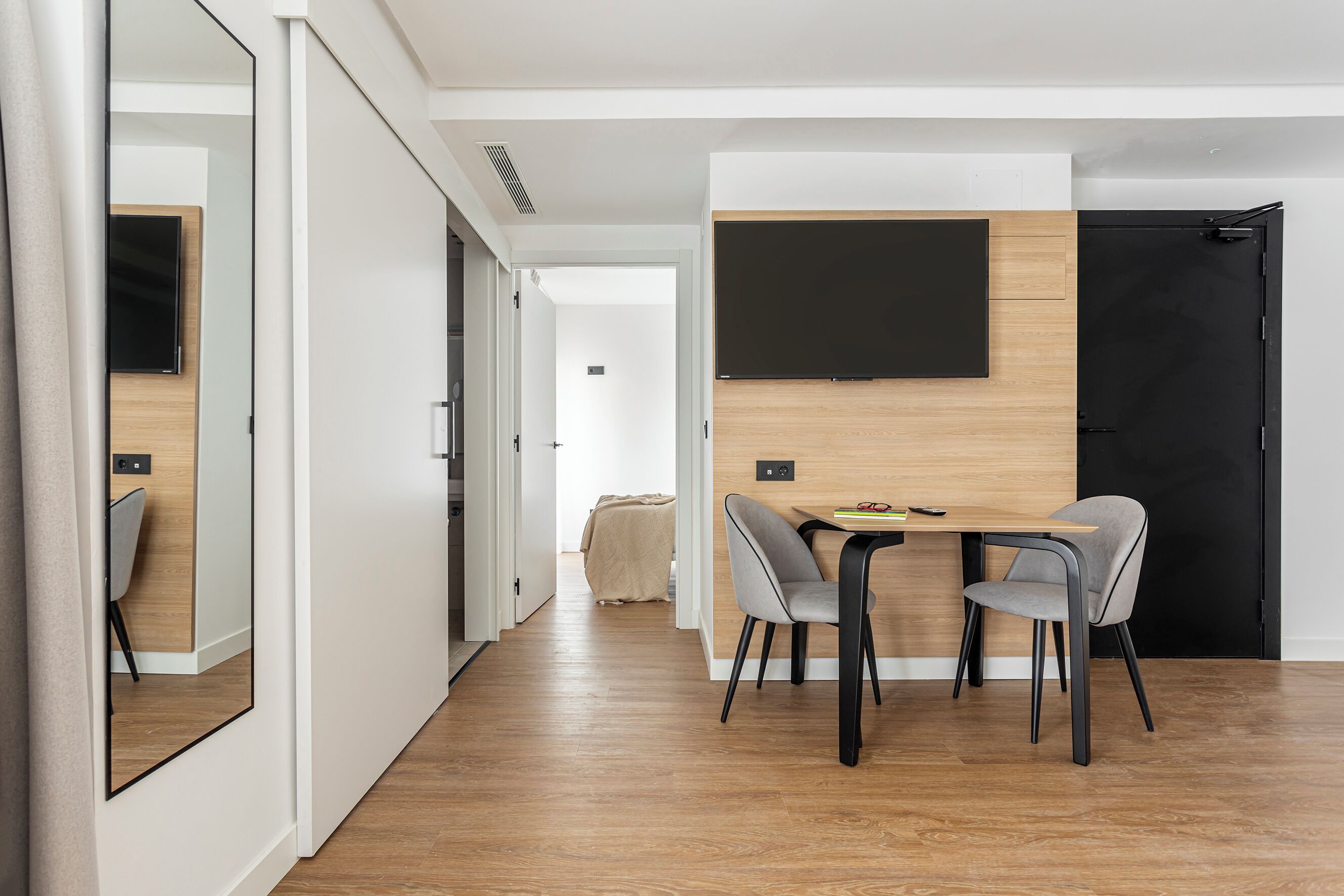 A modern dining area with a wooden table and two chairs, a blackboard on the wall, and a black door.