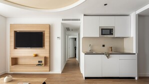 Una cocina moderna con armarios blancos, un microondas y un horno empotrado. Encima del mostrador hay un estante de madera con un televisor de pantalla plana.