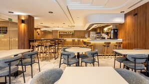 Un restaurante moderno con mesas redondas y sillas grises tapizadas, detalles de madera y una zona de bar.