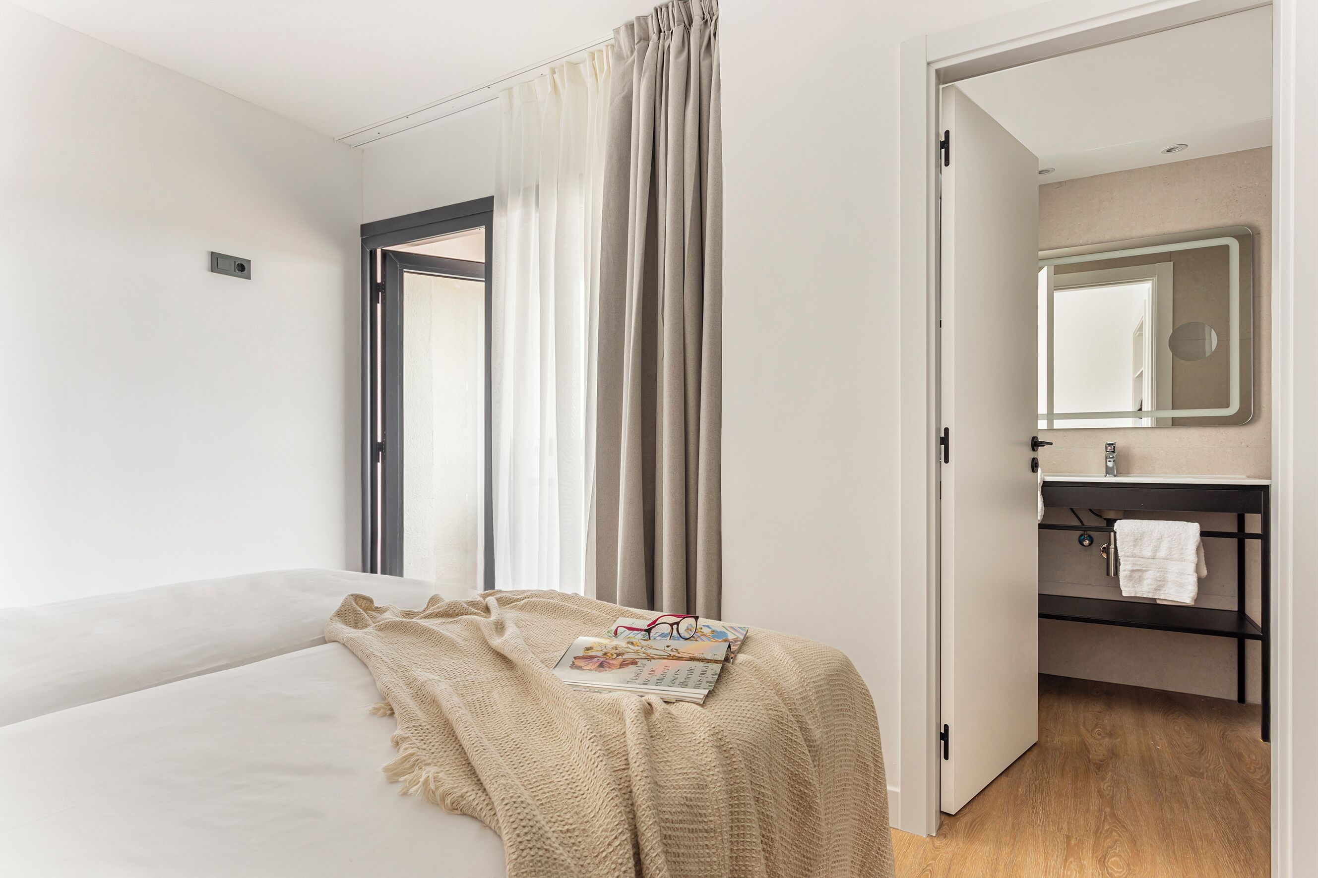 Habitación de hotel con una cama, un ventanal con cortinas, un baño con espejo y una toalla colgada en la puerta.