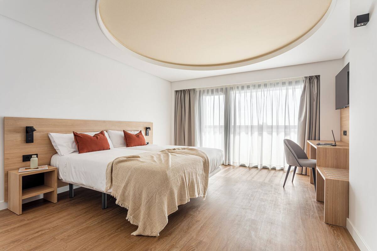 A modern hotel room with a wooden bed, a desk, and a chair.