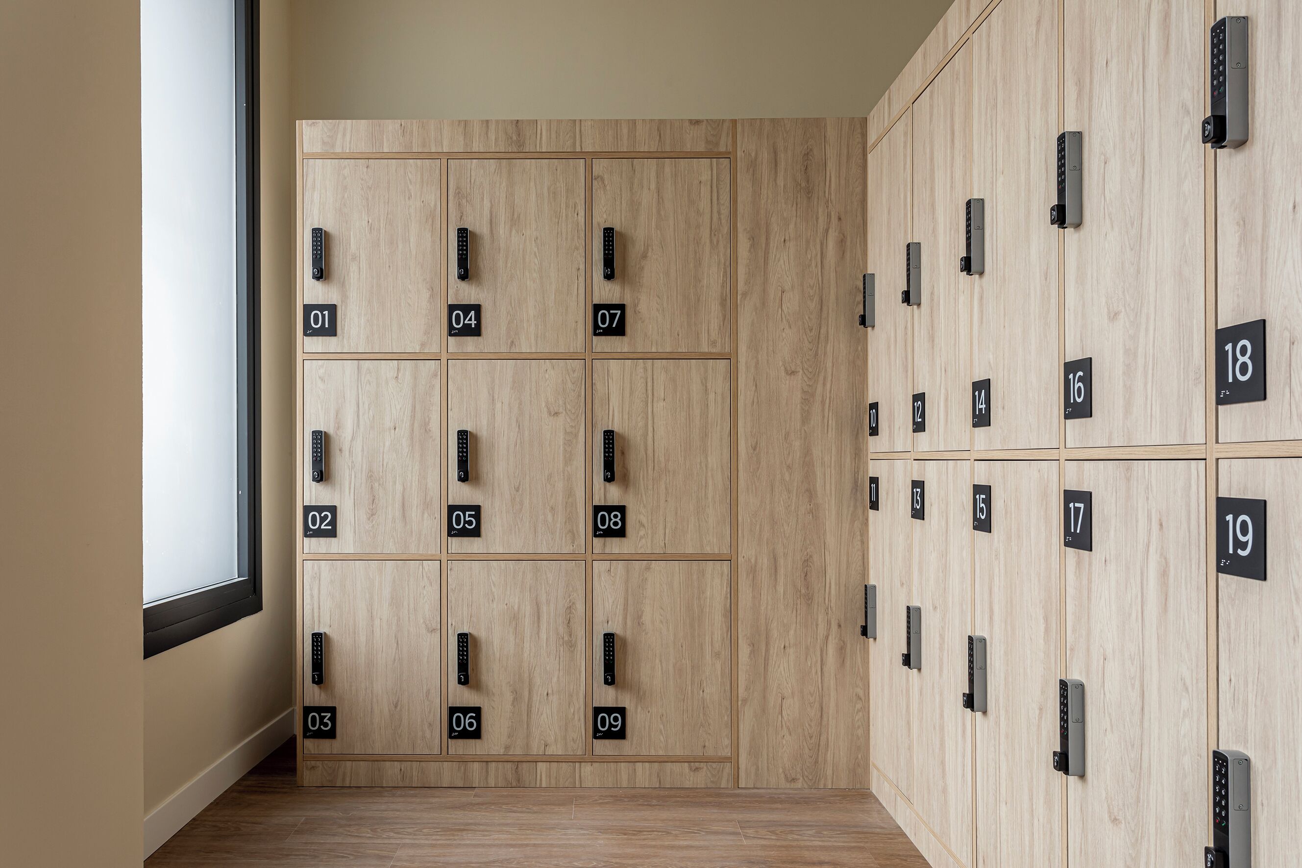 Habitación de hotel con taquillas de madera, numeradas del 01 al 19, y una ventana a la izquierda.