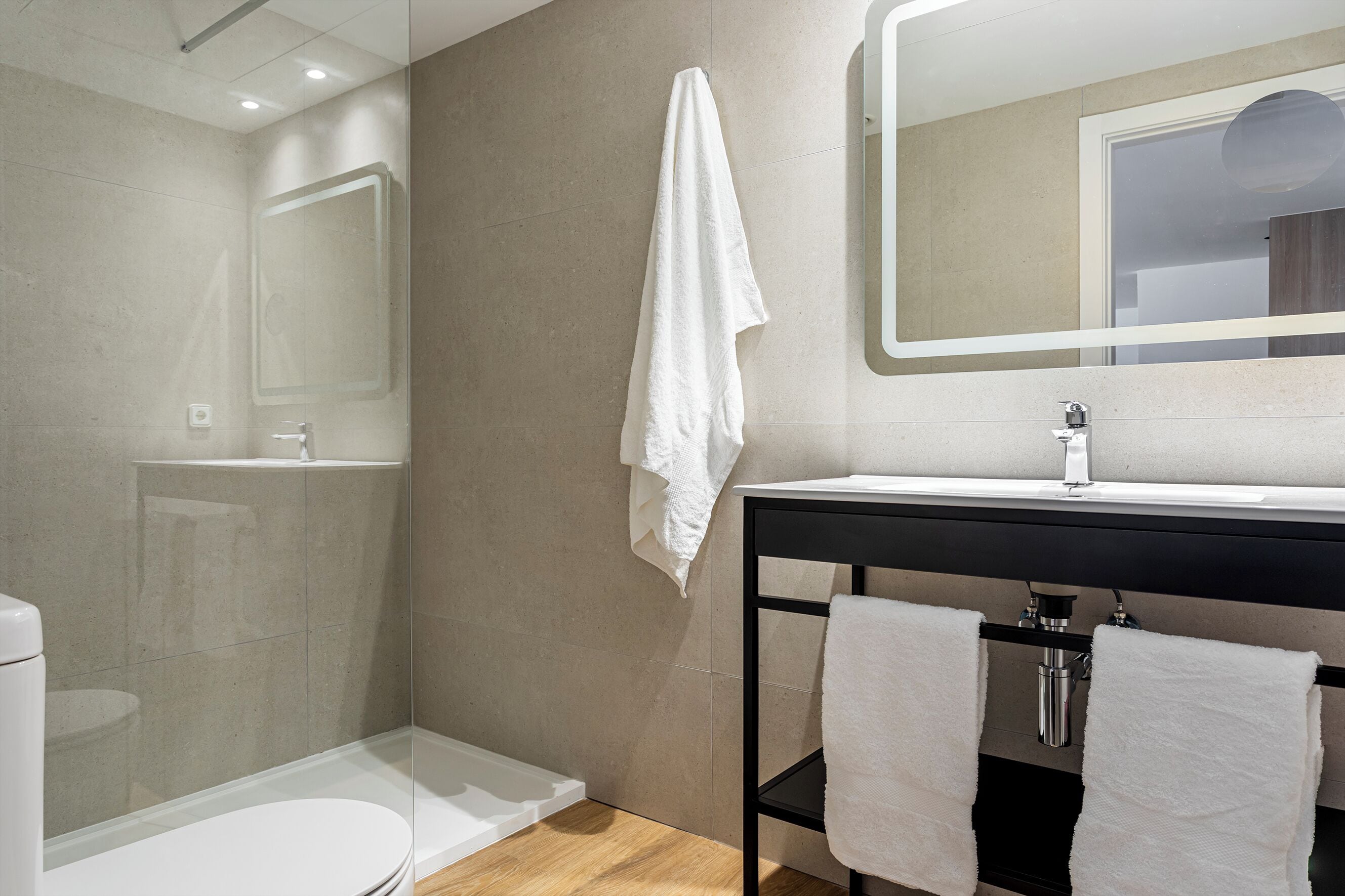 Un baño moderno con cabina de ducha de vidrio, inodoro blanco y lavamanos con espejo.