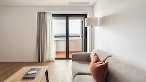 Habitación de hotel moderna con sofá, una mesa con un ordenador portátil y vistas al exterior a través de un ventanal grande.
