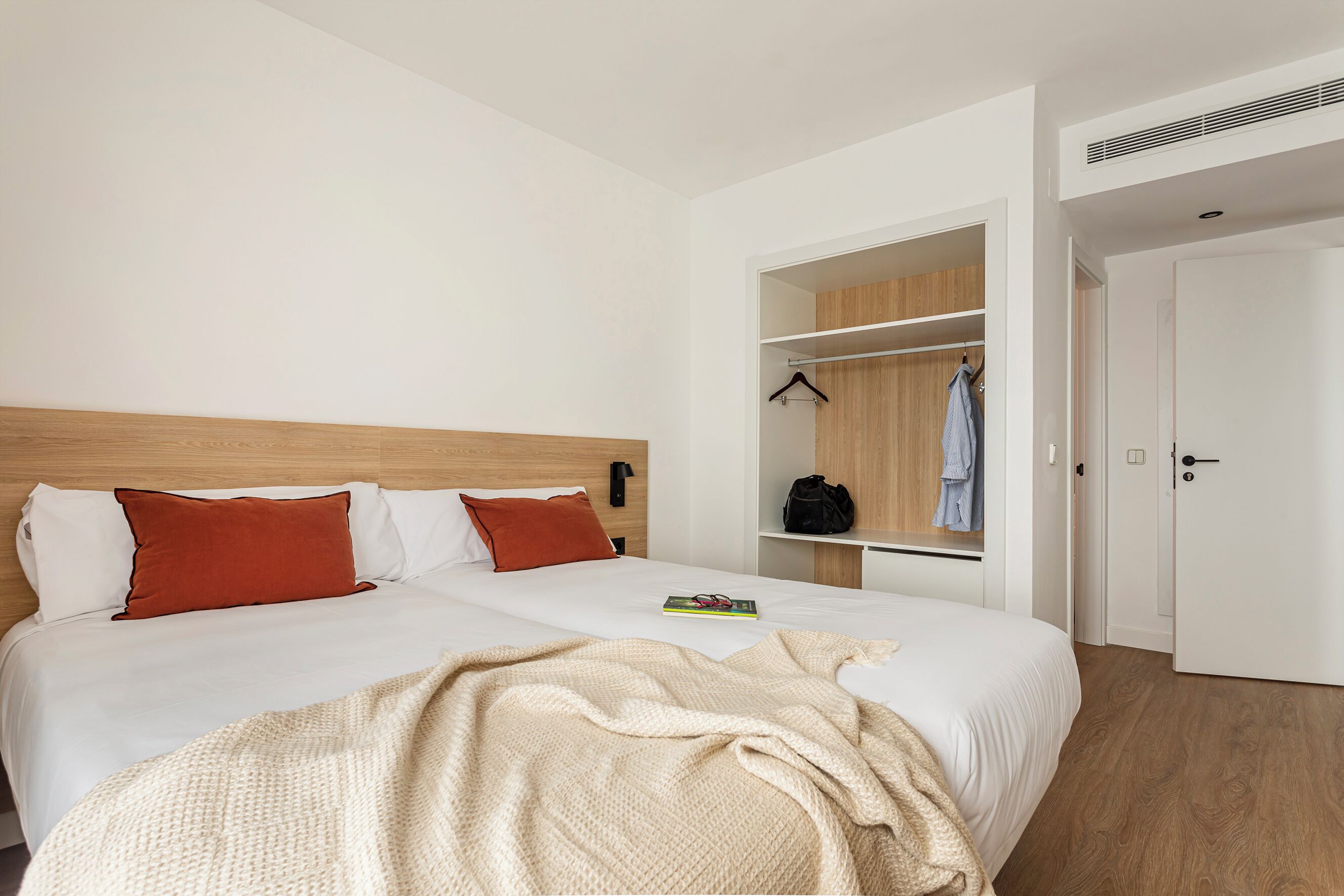 A hotel room with a large bed, a wardrobe with hanging clothes, and a door leading to another room.