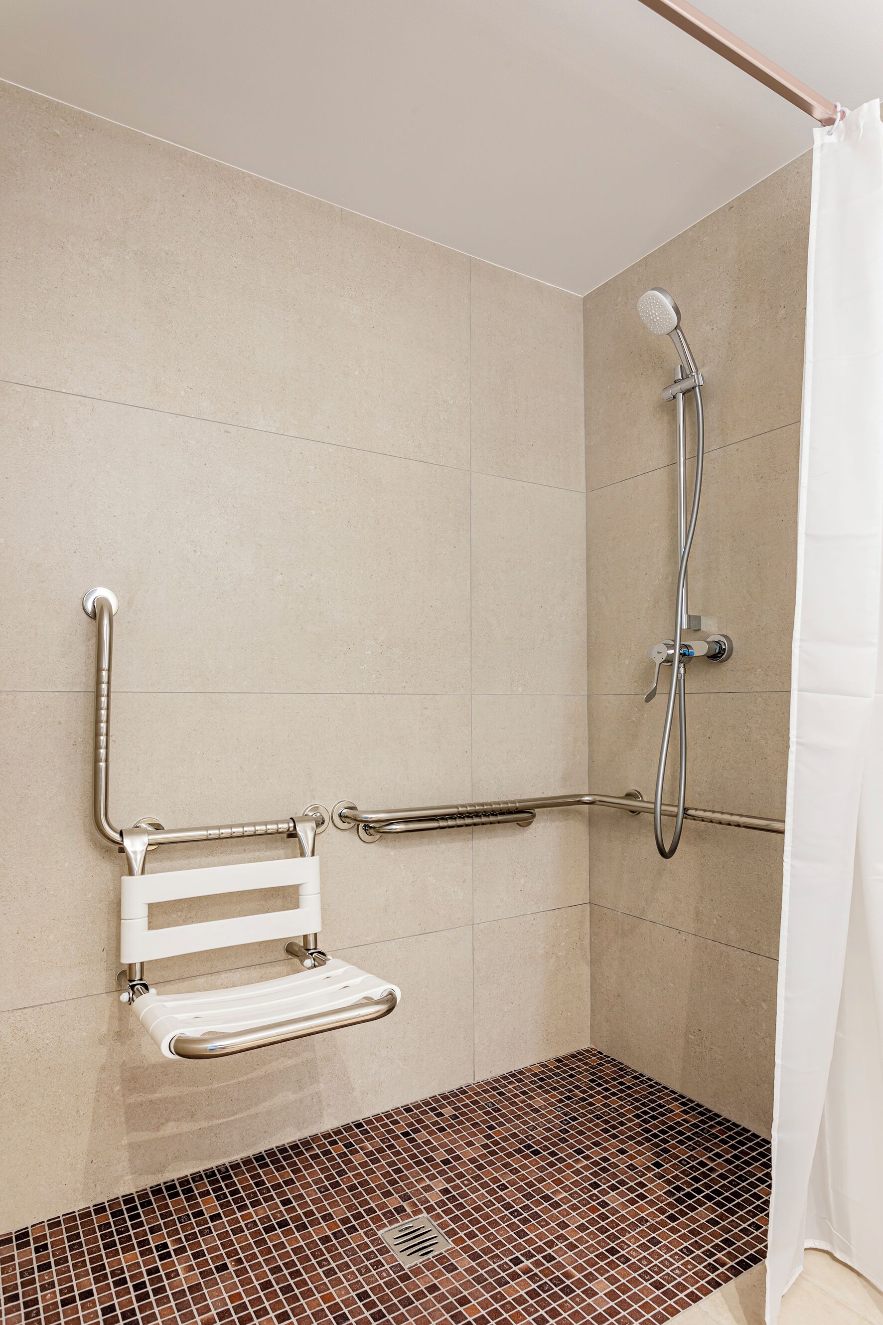 A shower area with a grab bar, a white towel rack, and a showerhead.