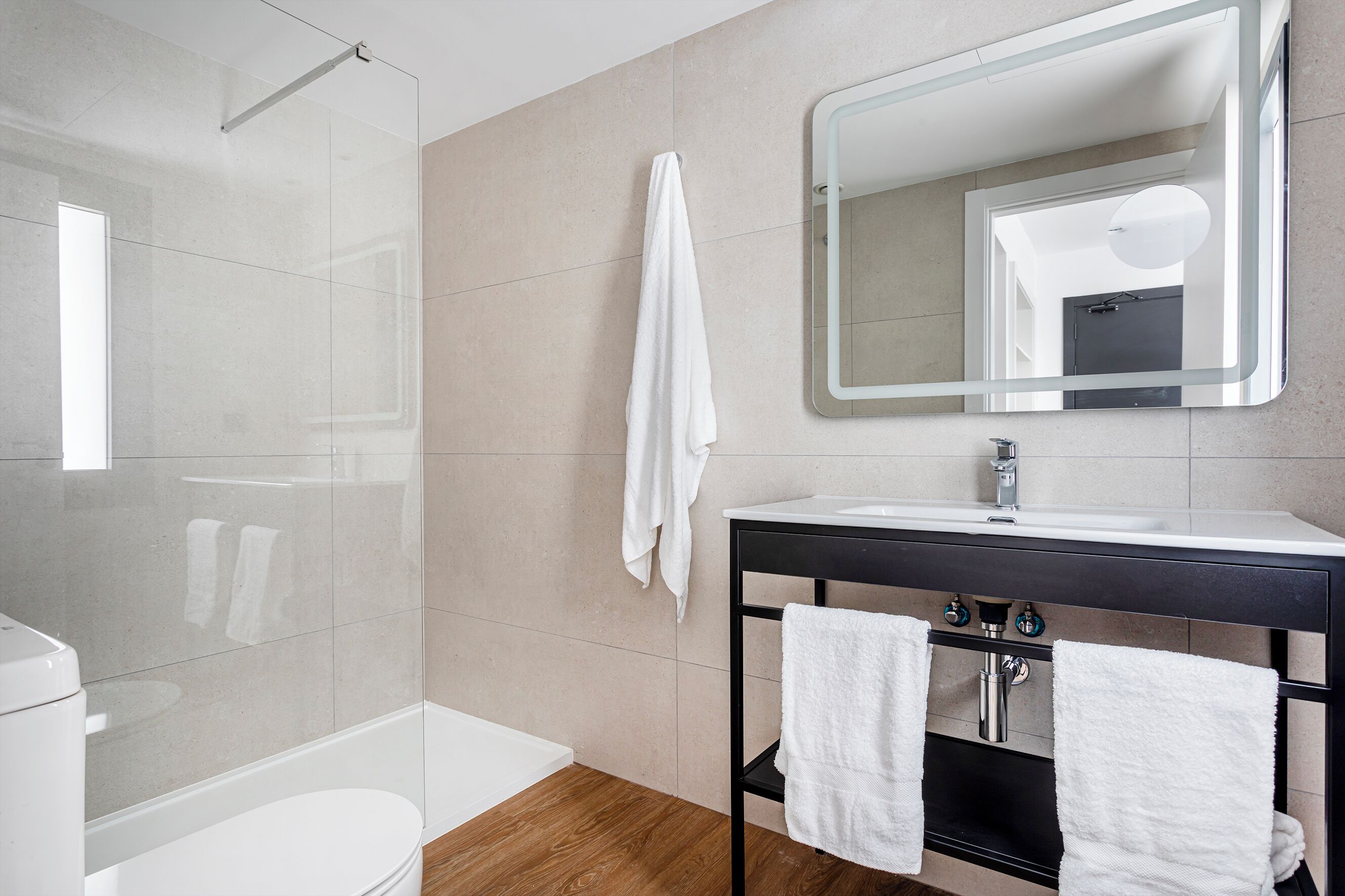 A modern bathroom with a glass shower, a white toilet, a sink with a mirror, and two towels hanging on a rack.