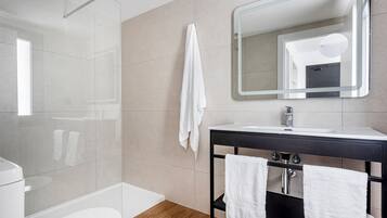 A modern bathroom with a glass shower, a white toilet, a sink with a mirror, and two towels hanging on a rack.