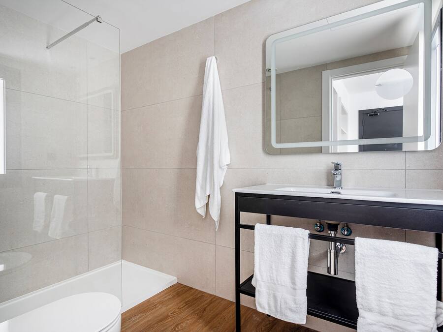 A modern bathroom with a glass shower, a white toilet, a sink with a mirror, and two towels hanging on a rack.